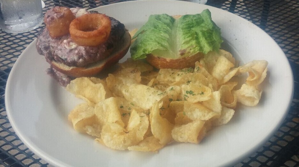 The Butter Bison Burger topped with house-made compound butter (Maytag bleu cheese, butter, bone marrow, red wine reduction), lettuce, onion rings, served on a pretzel roll.