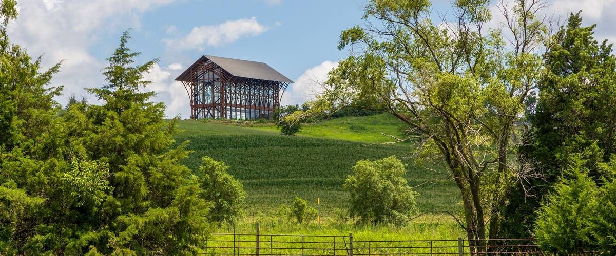 A modern building on a grassy hill with trees in the foreground.