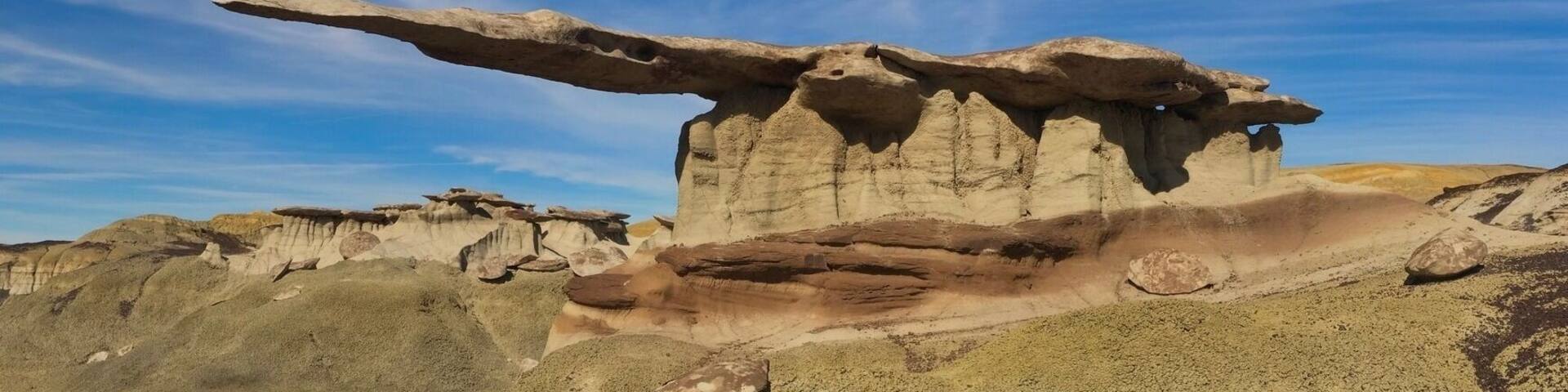 A rock formation with a prominent overhang in a desert landscape.