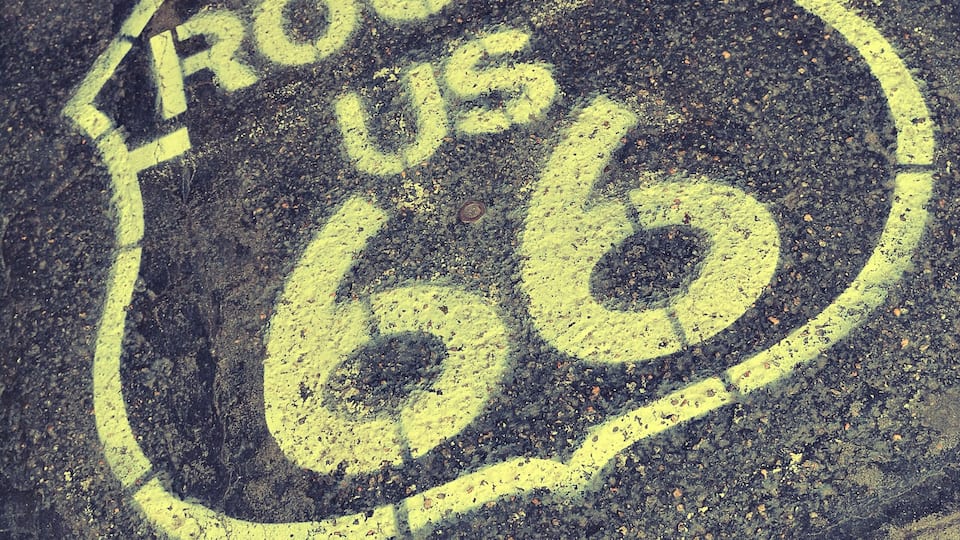 A faded Route 66 road sign on an asphalt surface.