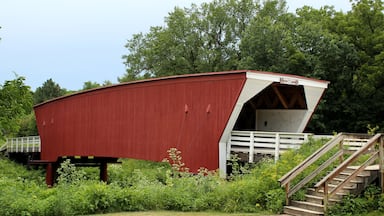 A red covered bridge with a white entrance, surrounded by greenery and a wooden staircase.