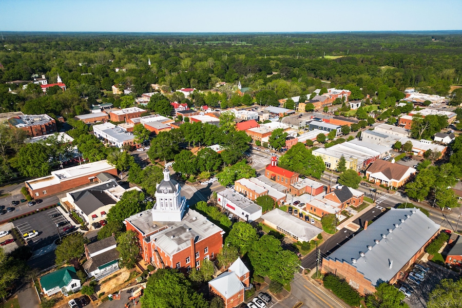 An aerial view of a town with historic buildings, a prominent church with a steeple, and surrounding greenery.