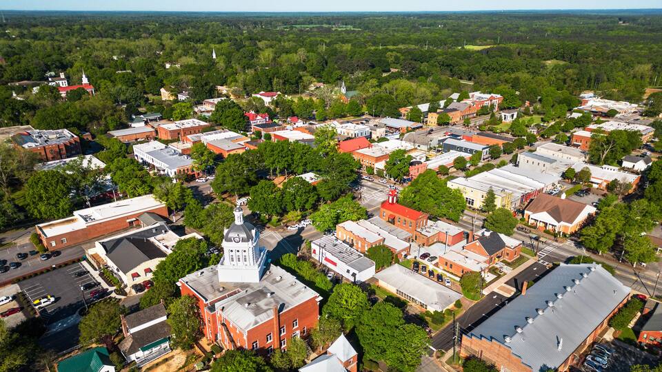 An aerial view of a town with historic buildings, a prominent church with a steeple, and surrounding greenery.