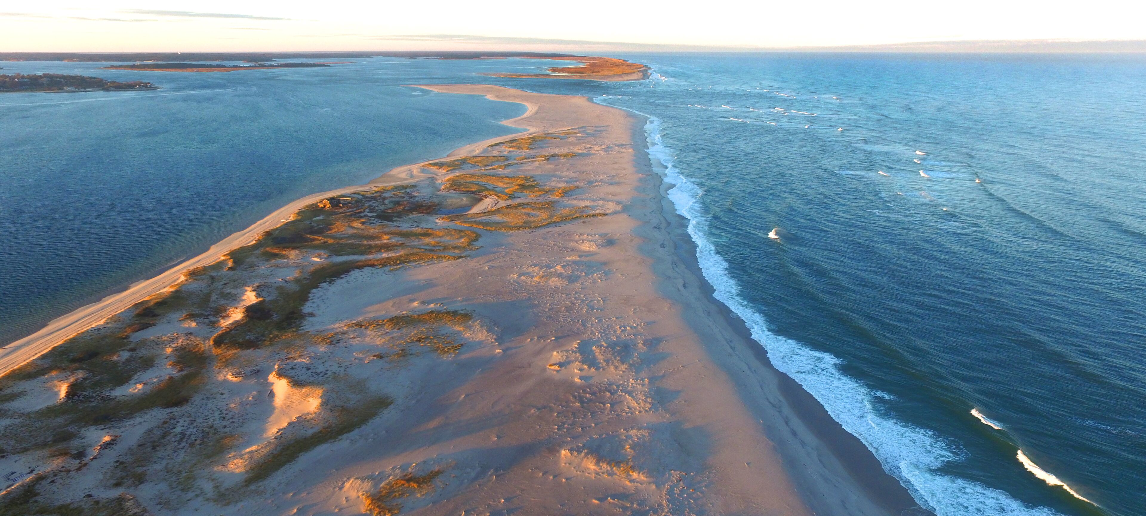 A coastal landscape with a sandy beach, a winding shoreline, and calm ocean waters.