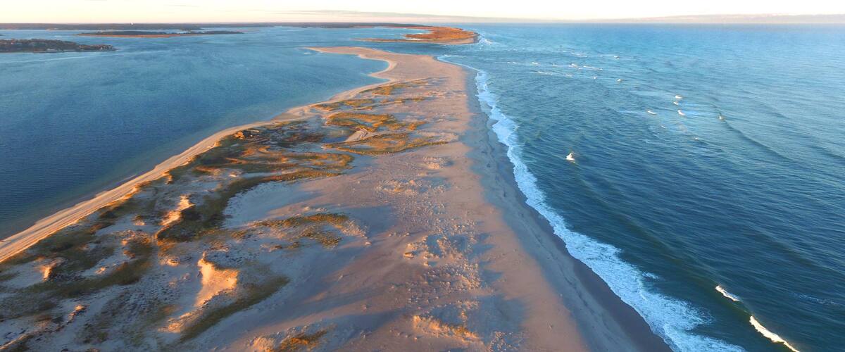 A coastal landscape with a sandy beach, a winding shoreline, and calm ocean waters.