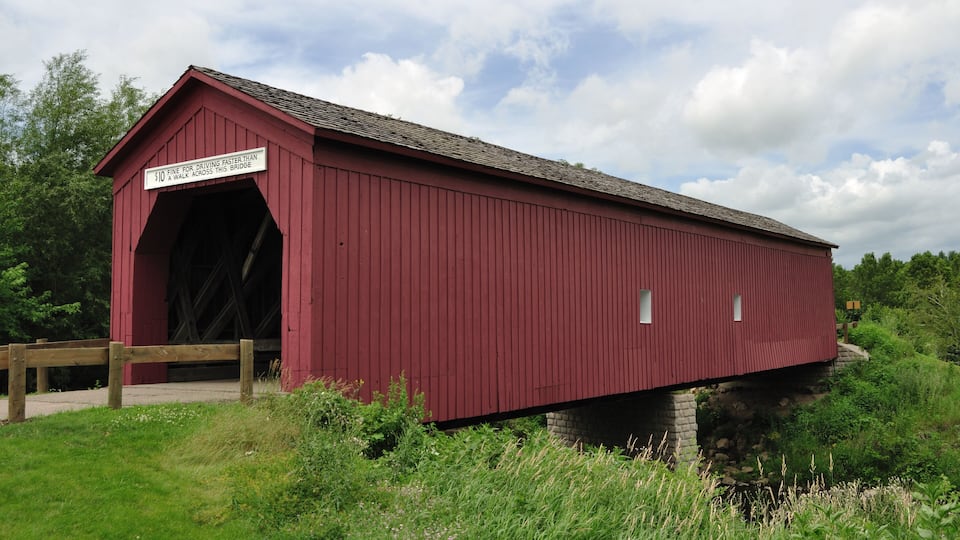 A red covered bridge with a sign warning against driving faster than a walk across.