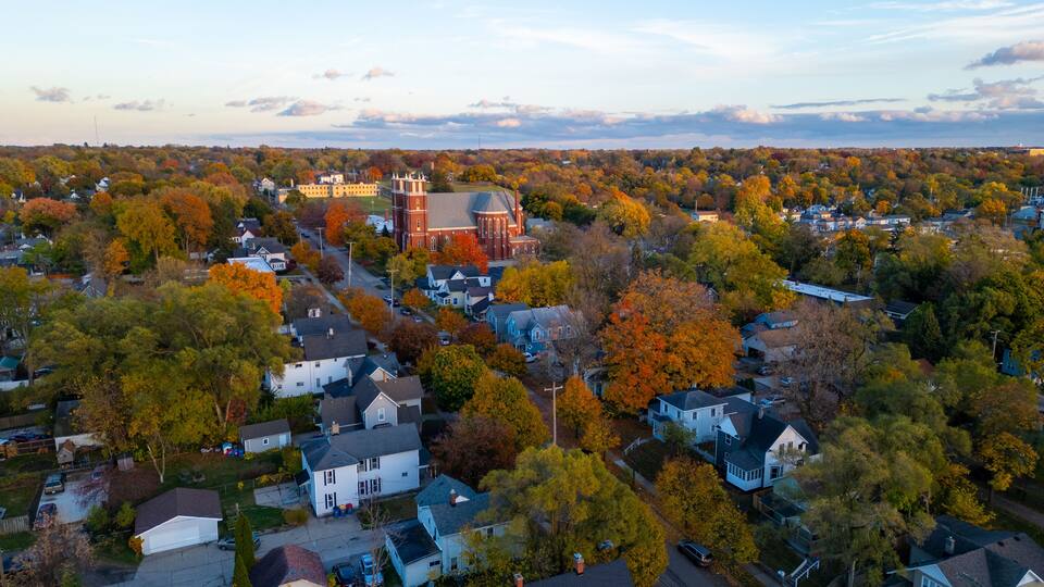 An aerial view of a town with autumn foliage, a prominent church, and residential houses.