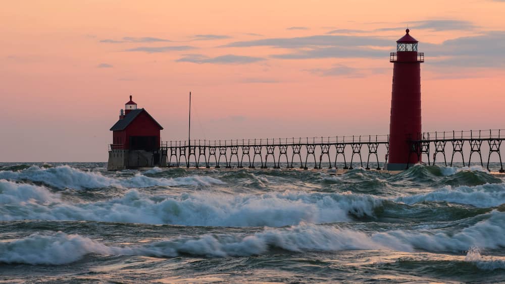 A red lighthouse and pier against a sunset sky.