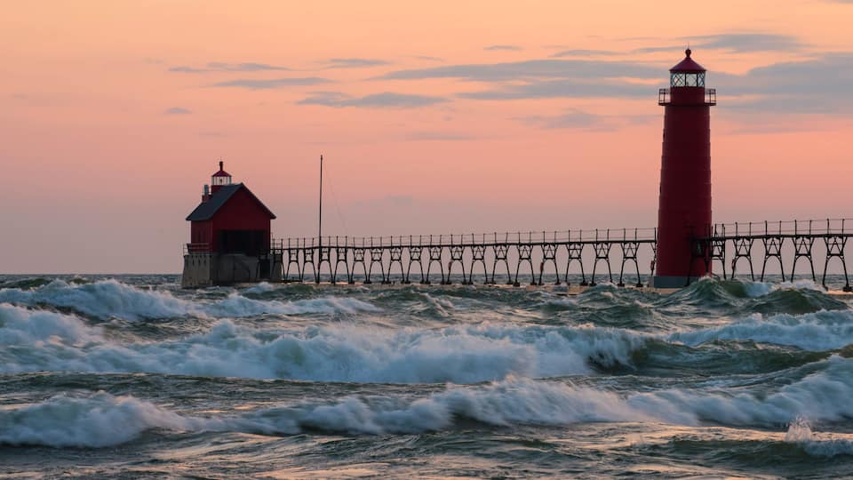 A red lighthouse and pier against a sunset sky.