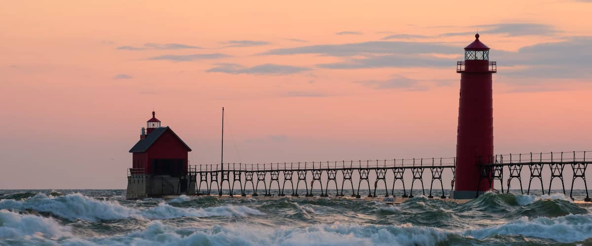 A red lighthouse and pier against a sunset sky.