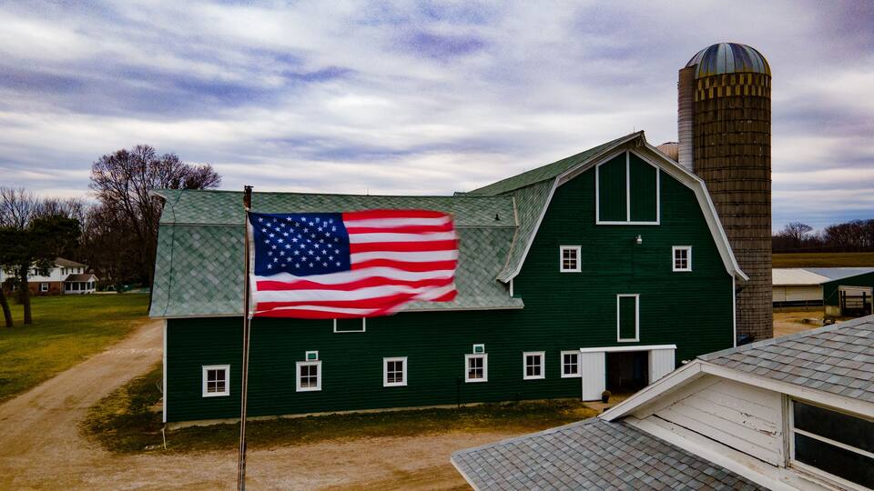 A green barn with a flagpole and an American flag.
