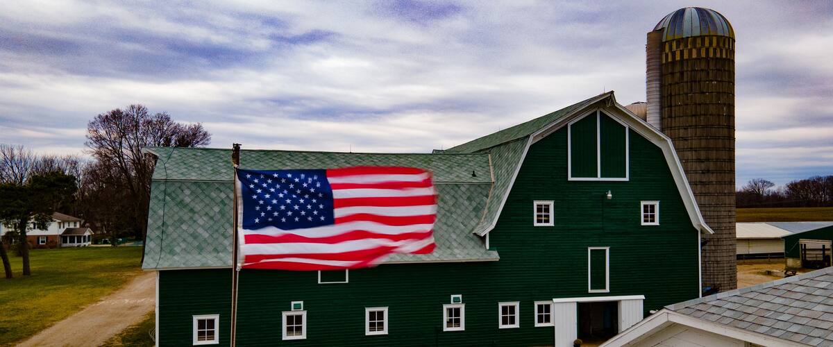 A green barn with a flagpole and an American flag.