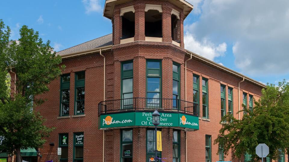 A brick building with a tower, a sign for Perham.com, and a sign for a raffle.