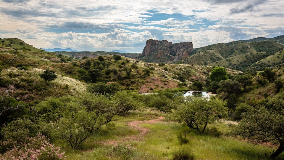 A valley with green hills, a rocky outcrop, and a small stream.