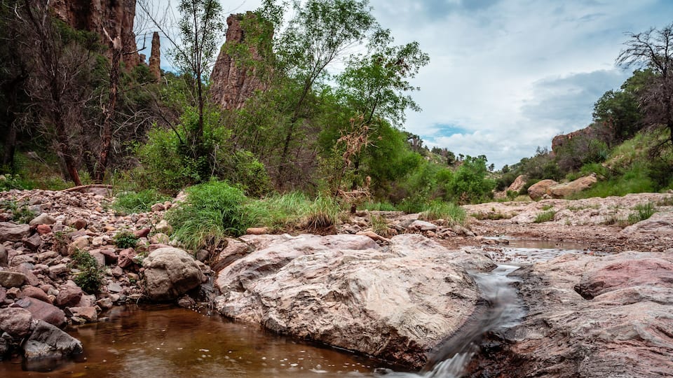 A rocky stream with a waterfall, surrounded by dense vegetation and cliffs.