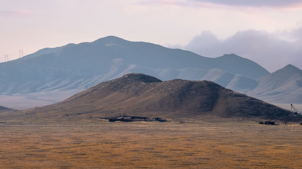 A mountainous landscape with a dry, grassy field and a few scattered buildings.