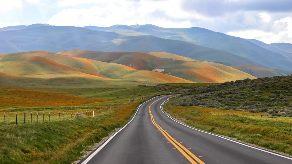 A winding road through rolling hills with a mountain range in the background.