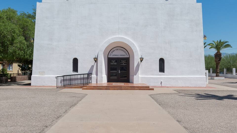 A white church with a cross on top, a bell tower, and a sign that reads "St. John the Evangelist Catholic Church".