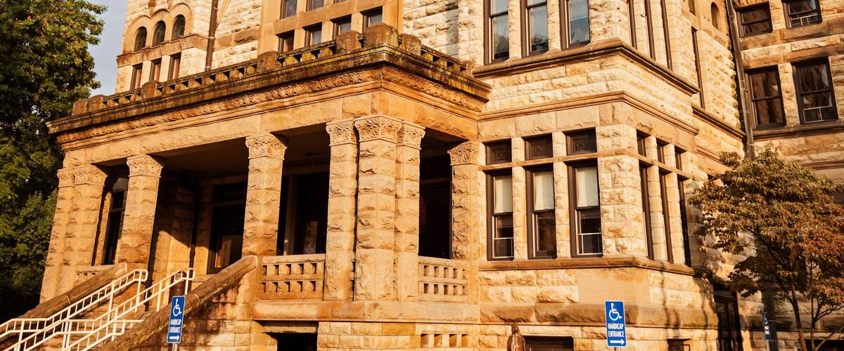 A historic stone building with a clock tower, large windows, and a prominent staircase.