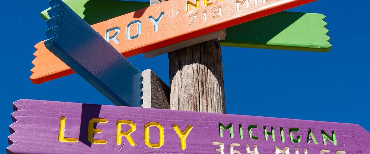 A wooden signpost with multiple directional signs pointing to various cities and distances.