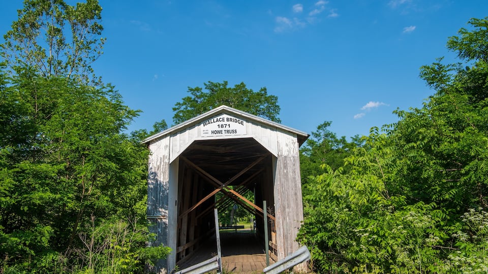 A dilapidated covered bridge with a sign reading "Wallace Bridge 1871 Howe Truss."