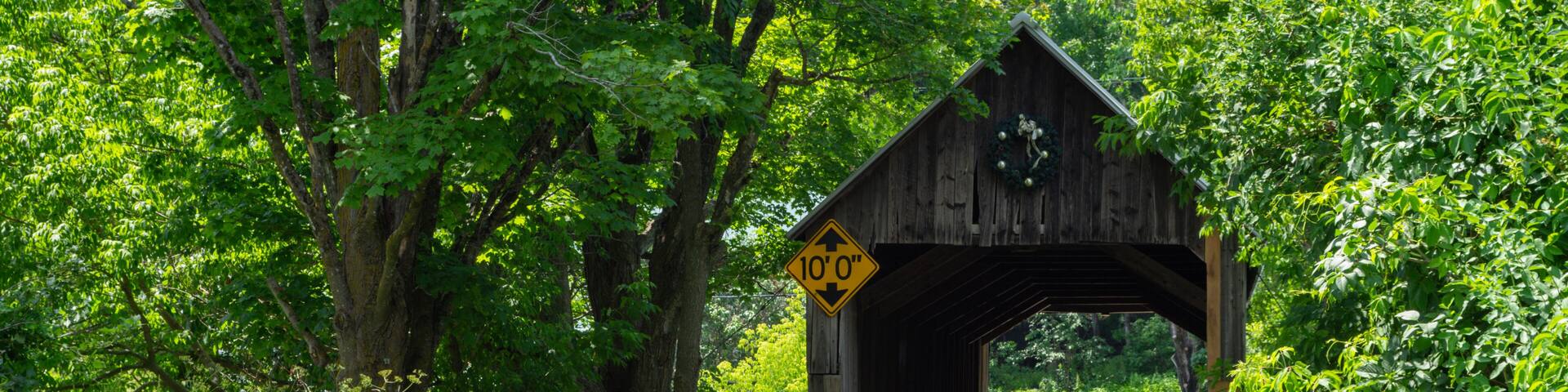 A wooden covered bridge with a 10'0' clearance sign, surrounded by lush greenery.