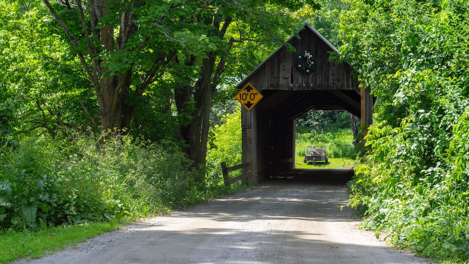 A wooden covered bridge with a 10'0' clearance sign, surrounded by lush greenery.