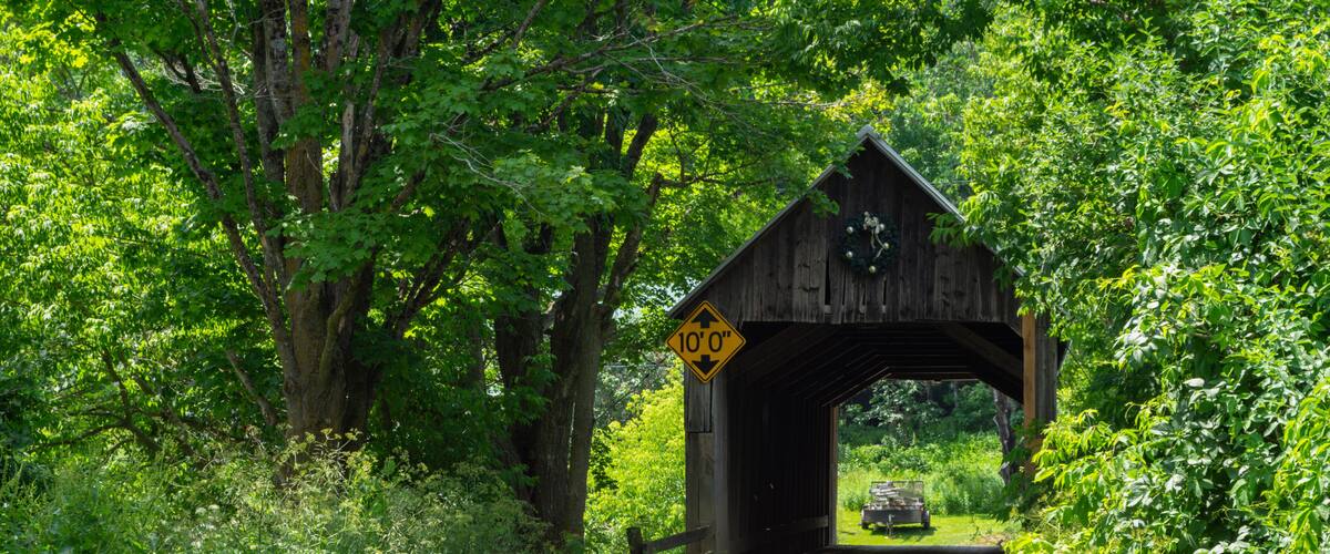 A wooden covered bridge with a 10'0' clearance sign, surrounded by lush greenery.