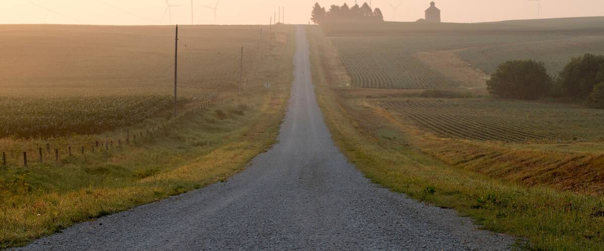 A rural road flanked by wind turbines and fields.