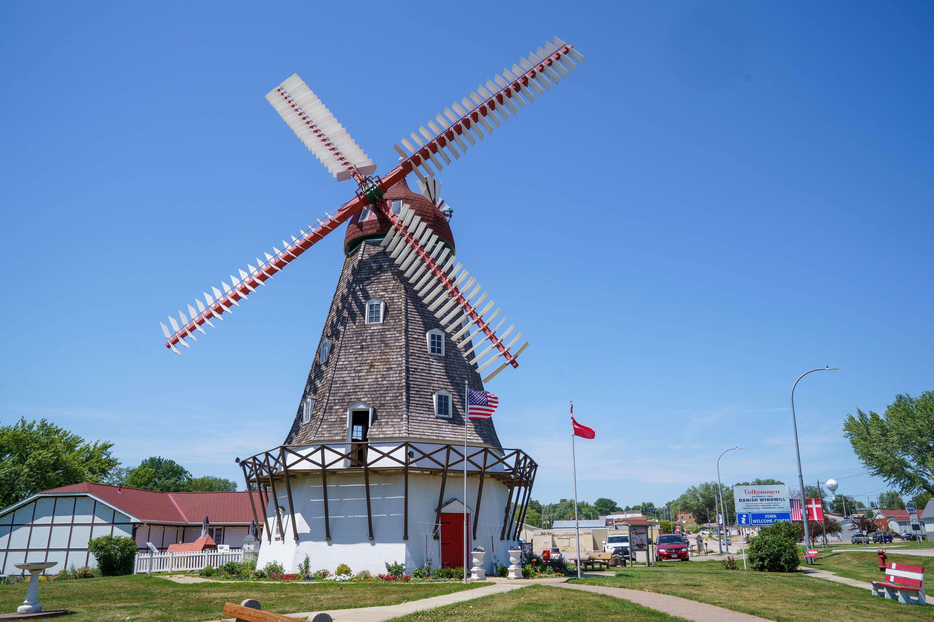 A traditional windmill with a red and white sail, surrounded by a white fence and a red door.