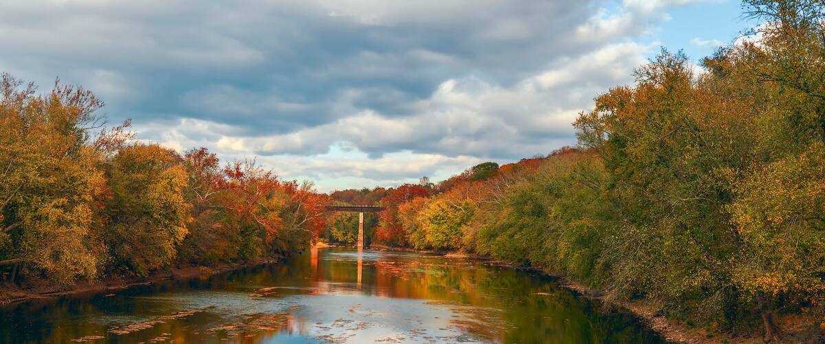 A river with autumn foliage, a bridge, and a cloudy sky.