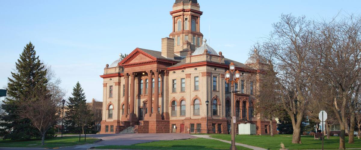 A large, historic building with a prominent dome and tower, surrounded by trees and a clear sky.