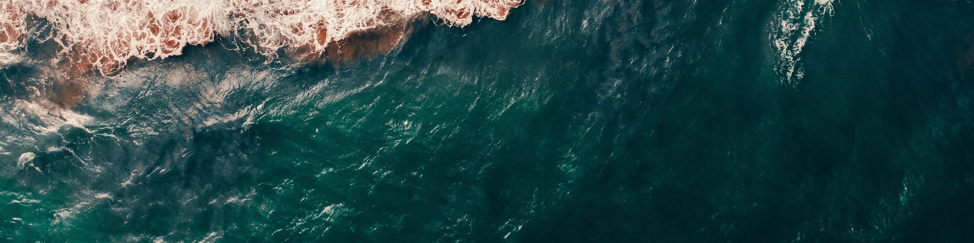 A large wave crashing onto a beach with a reddish hue.