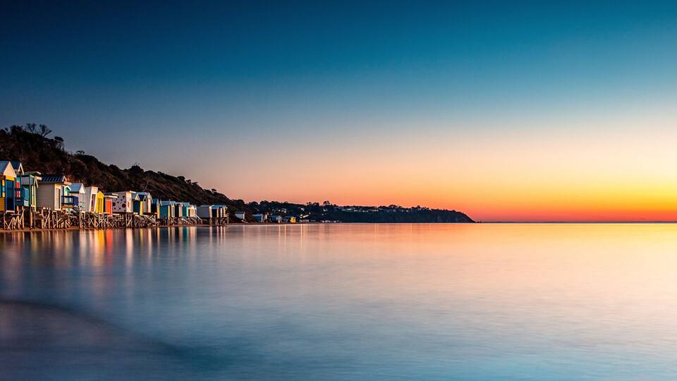 Cena costeira com cabanas de praia coloridas e mar calmo ao pôr do sol.
