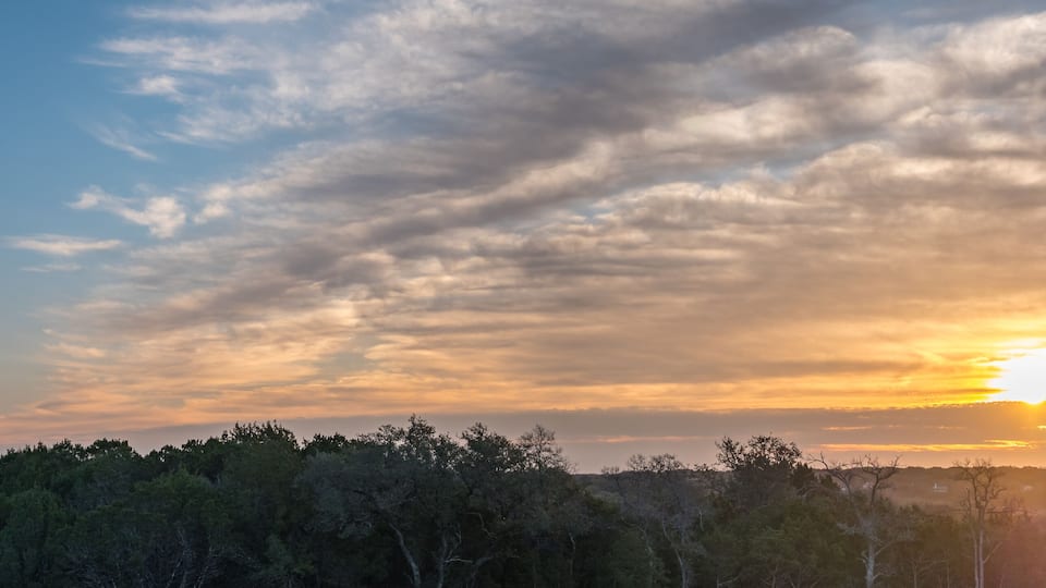 A sunset over a forested landscape with a clear sky and scattered clouds.