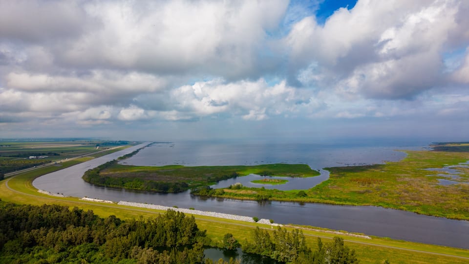 A river meandering through a landscape with dense forests and open fields, under a partly cloudy sky.