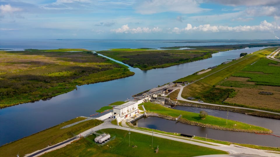 An aerial view of a coastal landscape with a river, green fields, and a large industrial facility.