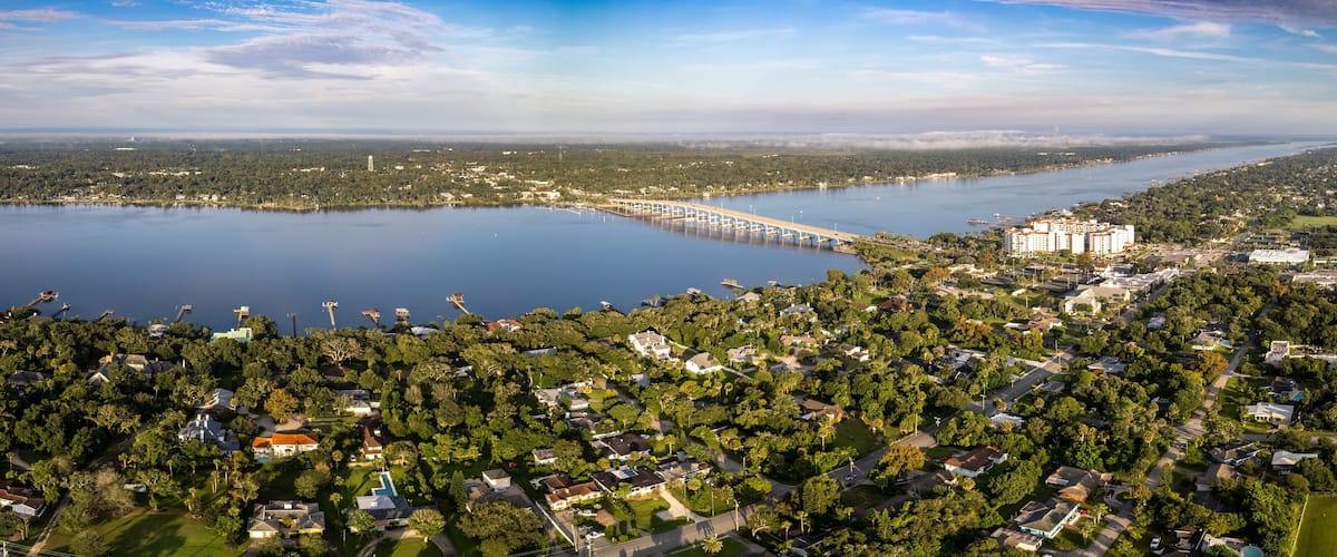 A lake with a bridge, a large building, and a densely wooded area.