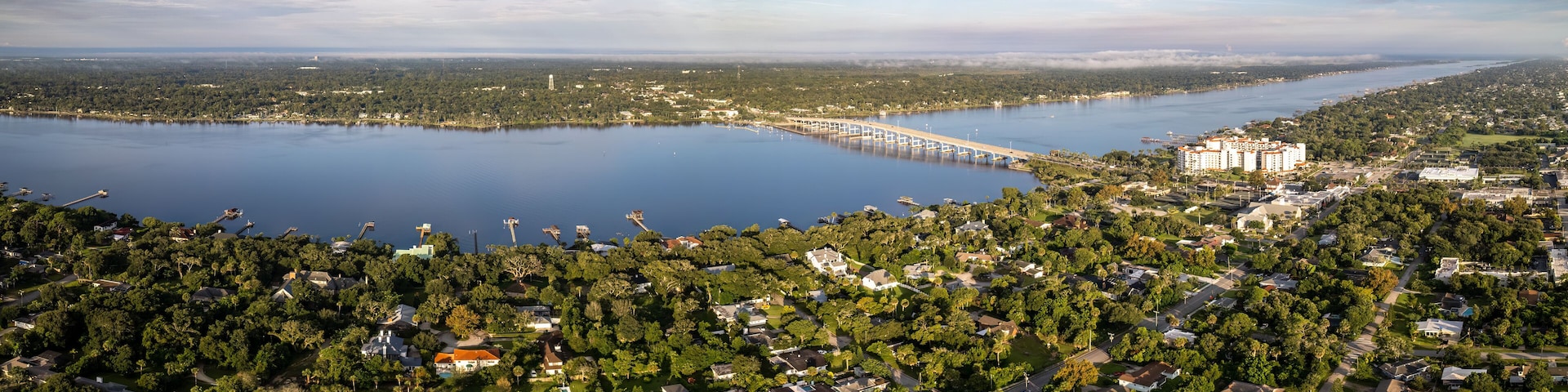 A lake with a bridge, a large building, and a densely wooded area.