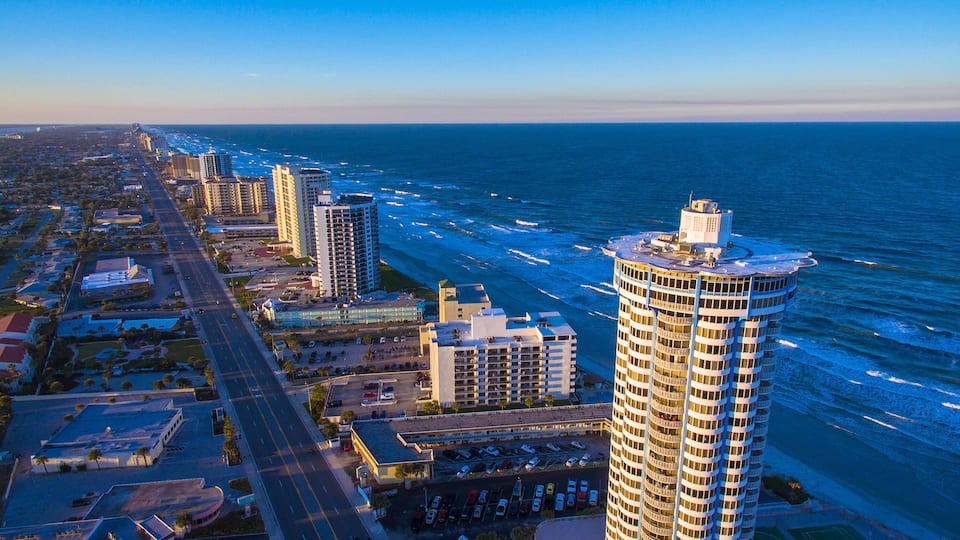 A coastal cityscape with high-rise buildings, a wide road, and the ocean.