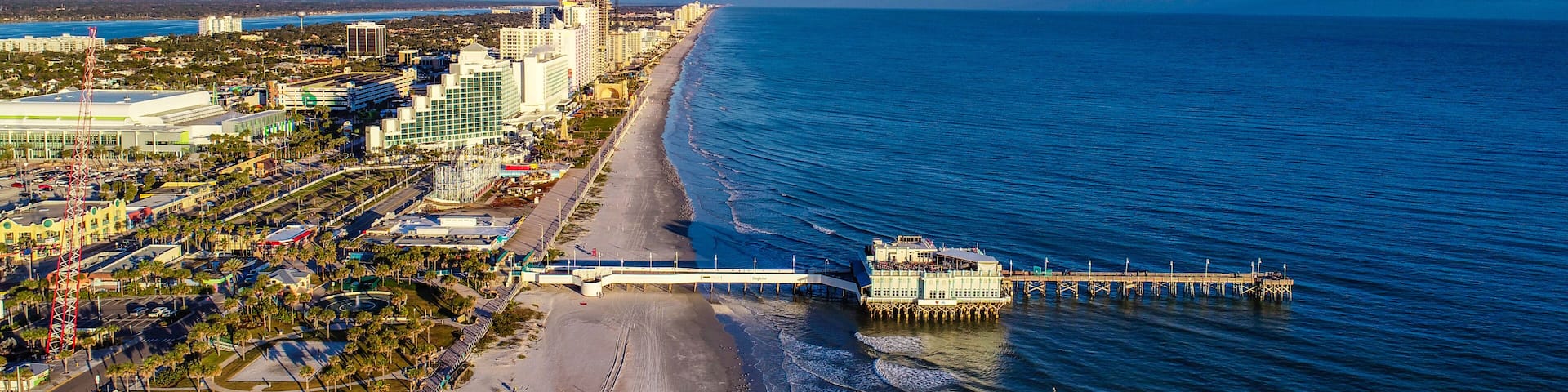 A coastal cityscape with a beach, pier, and high-rise buildings.