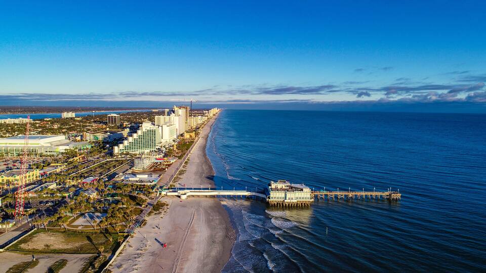 A coastal cityscape with a beach, pier, and high-rise buildings.