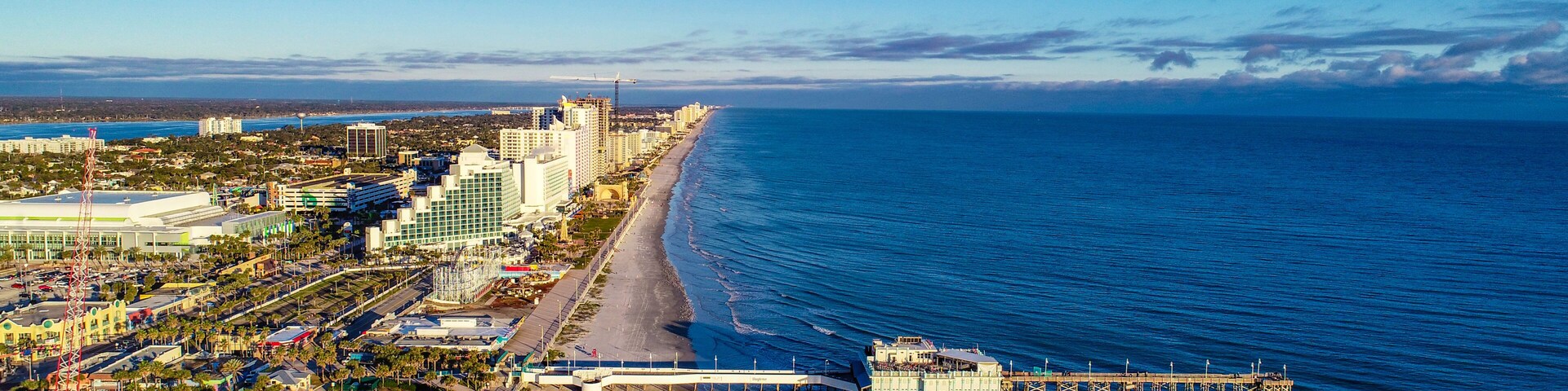 Paisagem costeira com praia, píer e edifícios altos.