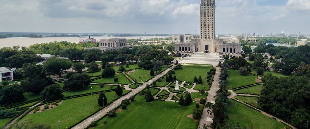 A large, historic building with a tall tower, surrounded by well-maintained gardens and a river in the background.