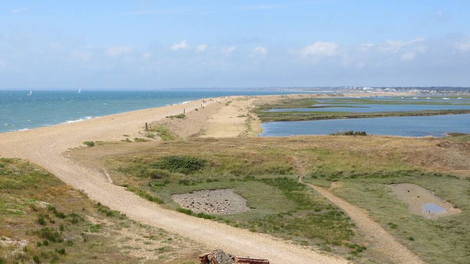 A coastal landscape with a sandy beach, a dirt path, and a body of water.