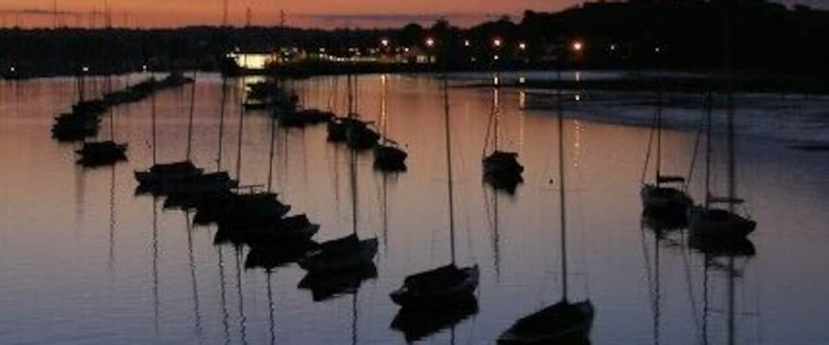 Boats moored on the river, Lymington These boats are moored on the river at Lymington, the Isle of Wight ferry channel passes to the left of the boats, heading for the brightly lit ferry terminal in the distance. Viewed from the ferry as it returns from Yarmouth.