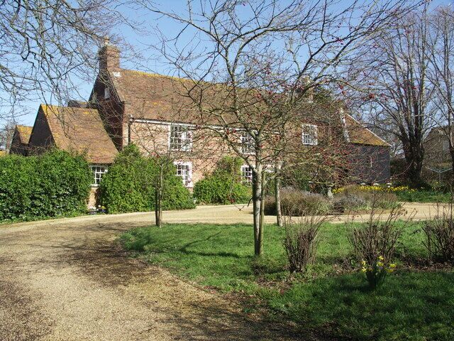 A large brick house with a sloped roof, surrounded by a well-maintained garden and a gravel driveway.