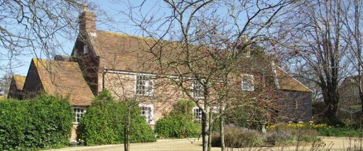 A large brick house with a sloped roof, surrounded by a well-maintained garden and a gravel driveway.