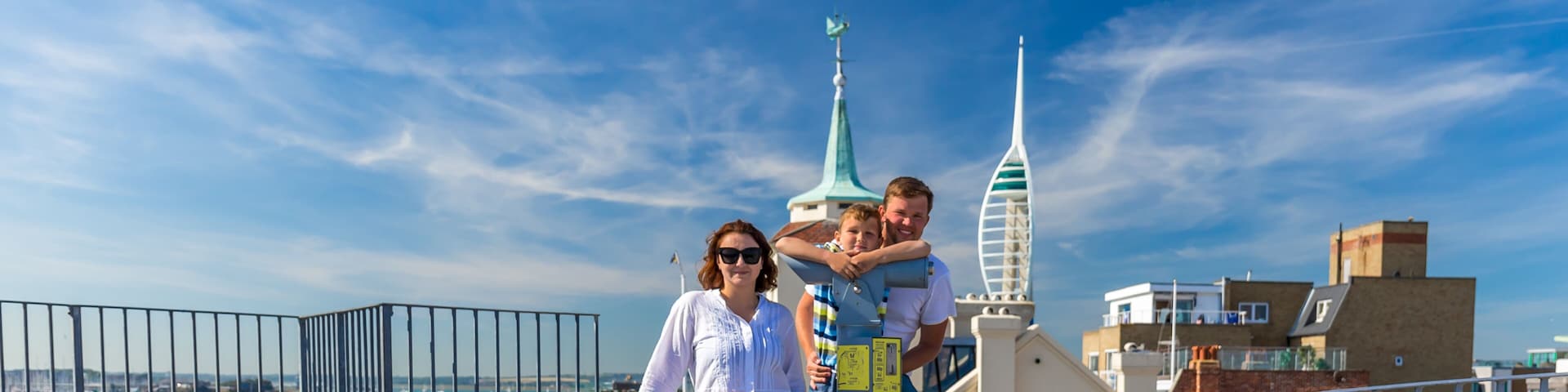 A coastal promenade with a metal railing, a statue, and a clear blue sky.