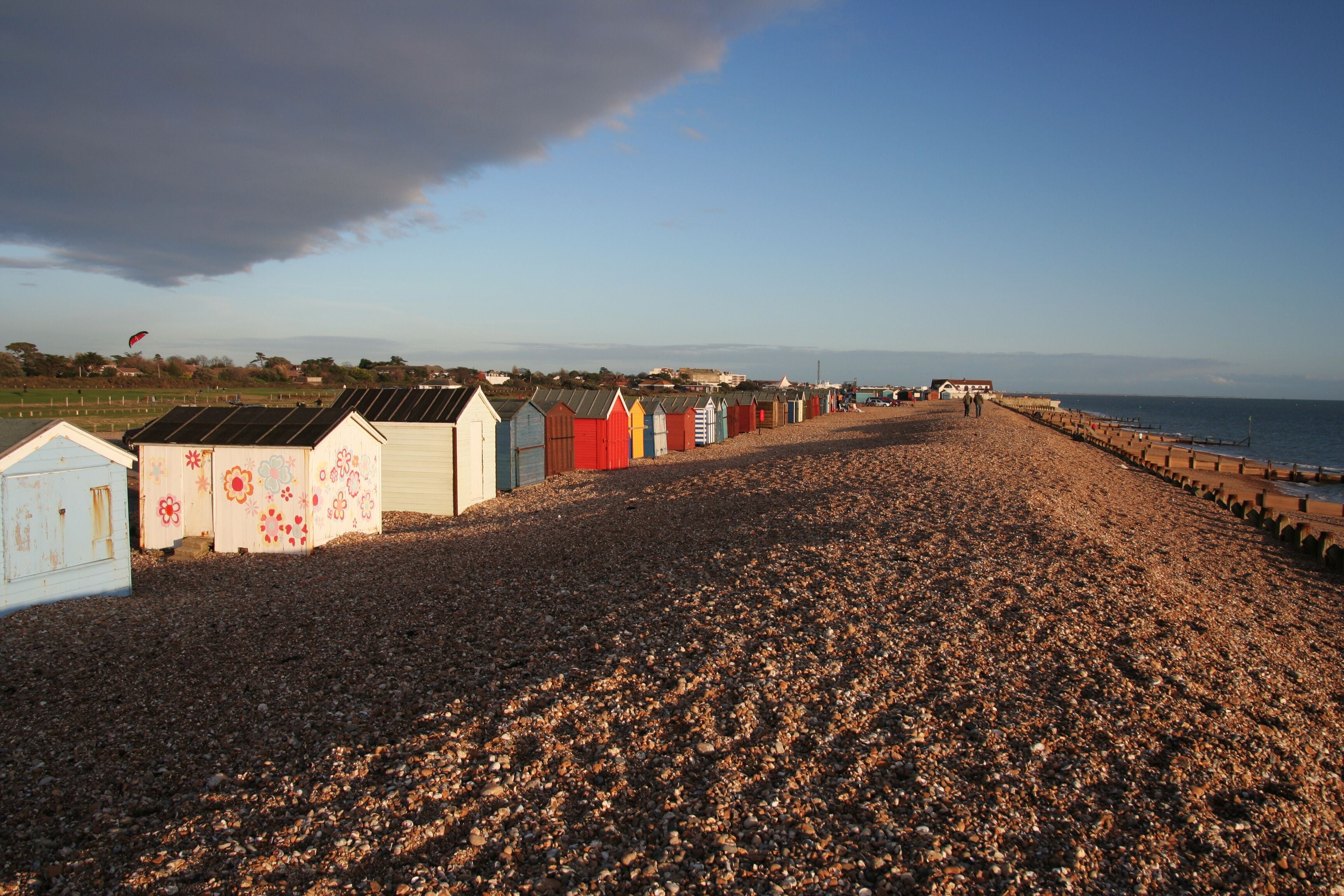 A pebbled beach with colorful beach huts and a clear sky.